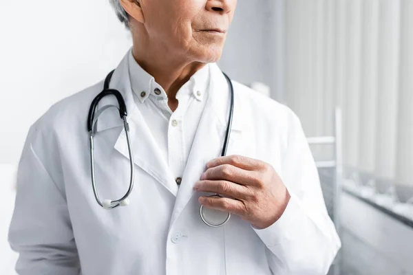 Vista recortada del médico senior sosteniendo estetoscopio en la clínica - foto de stock