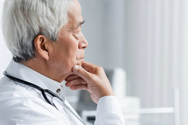 Вид збоку на старшого азіатського лікаря, який дивиться в клініку — стокове фото