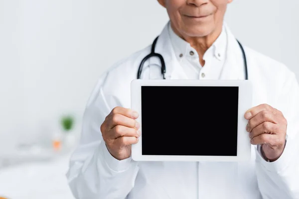 Обрізаний вид цифрового планшета з порожнім екраном в руках розмитого лікаря в клініці — стокове фото