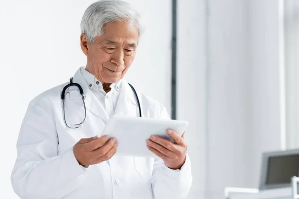 Médecin asiatique senior regardant tablette numérique à l'hôpital — Photo de stock