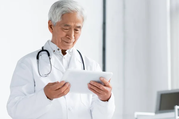 Senior asian doctor looking at digital tablet in hospital — Stock Photo
