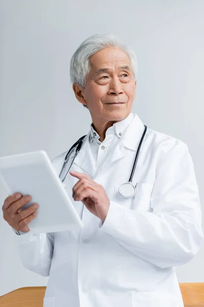 Sénior asiático médico em casaco branco segurando tablet digital no hospital — Fotografia de Stock