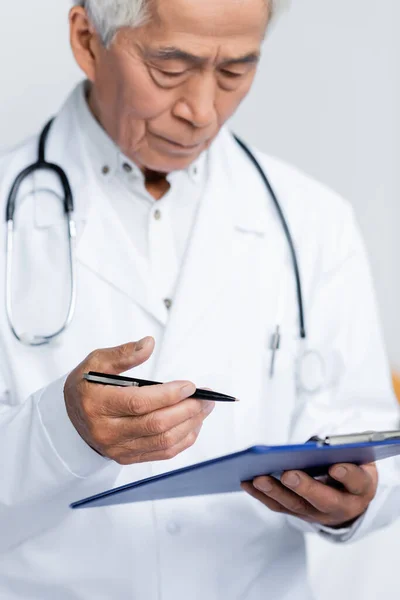 Borrosa asiático médico holding pluma y portapapeles en clínica - foto de stock