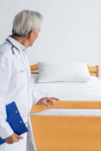 Médico desfocado com área de transferência olhando para a cama na enfermaria do hospital — Fotografia de Stock