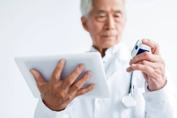 Laptop e oxímetro de pulso em mãos de médico asiático desfocado na clínica — Fotografia de Stock