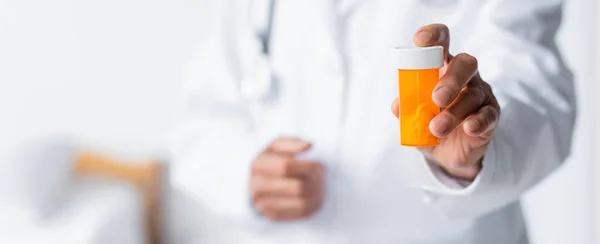 Обрізаний вид баночки з таблетками в руці розмитого лікаря в лікарні, банер — стокове фото