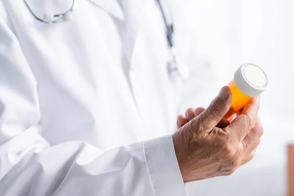 Cropped view of senior doctor holding jar with pills in hospital — Stock Photo