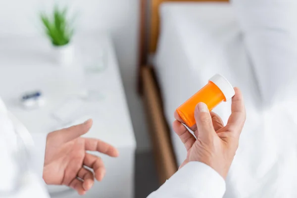 Vista recortada del médico sosteniendo frasco con pastillas en la sala de hospital - foto de stock