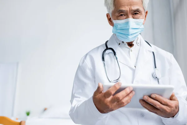 Älterer asiatischer Arzt in medizinischer Maske mit digitalem Tablet im Krankenhaus — Stockfoto