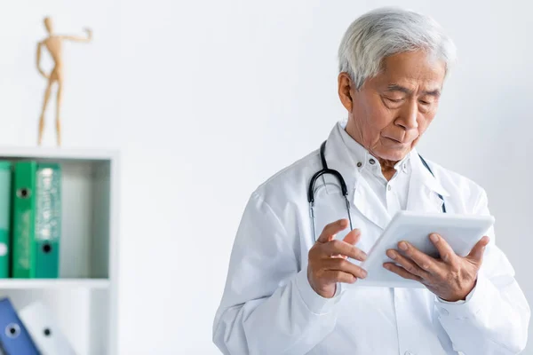 Senior asiático médico usando digital tablet mientras trabajo en clínica - foto de stock