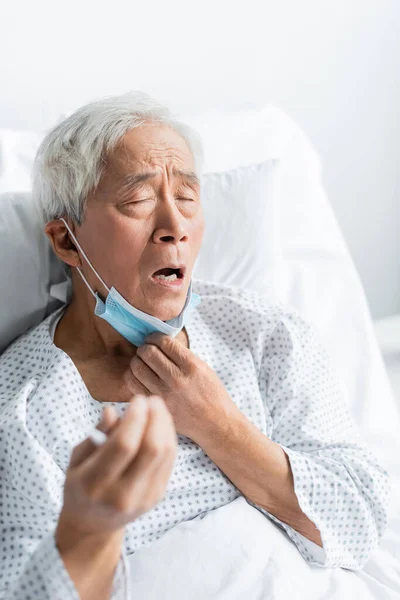 Paciente asiático enfermo con máscara médica sentado en la cama en la sala de hospital - foto de stock