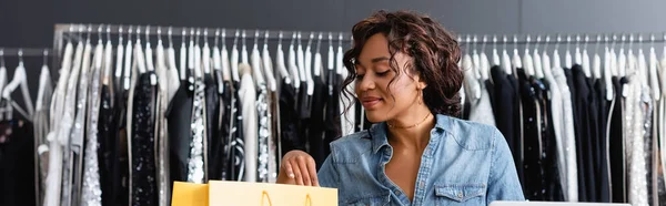 Alegre afroamericana vendedora mirando bolsa de papel amarillo, pancarta - foto de stock