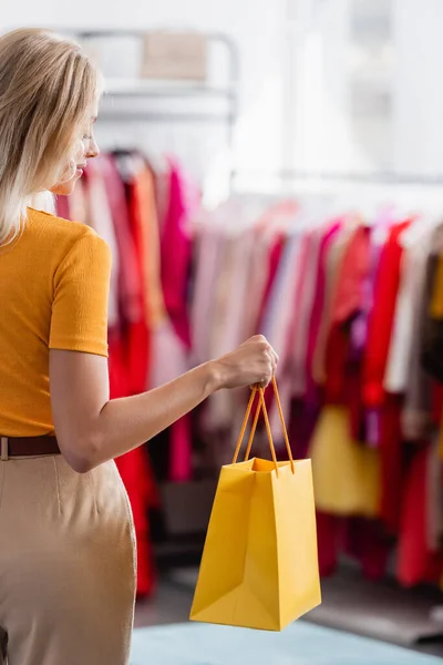 Donna sorridente guardando la shopping bag gialla nella boutique di abbigliamento — Foto stock