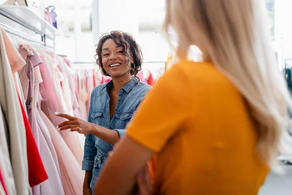 Feliz africano americano tienda asistente mirando borrosa cliente en boutique - foto de stock