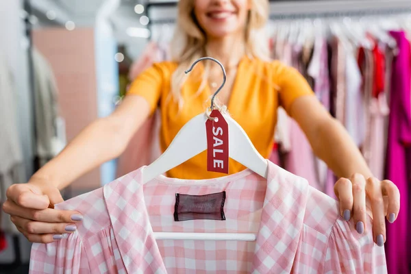 Cropped view of happy woman holding hanger with checkered pink dress and sale tag — Stock Photo