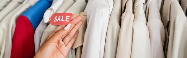 Vista recortada de africano americano tienda asistente celebración venta etiqueta cerca de la ropa en boutique, pancarta — Stock Photo