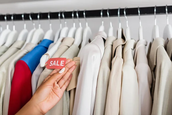 Cropped view of african american woman holding sale tag near clothing in boutique — Stock Photo