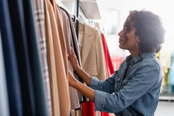 Vista laterale della donna riccia africana americana che guarda i vestiti in boutique — Foto stock