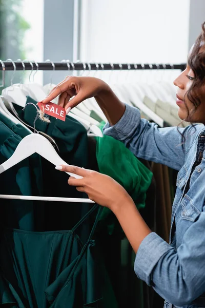 Afrikanisch-amerikanische Verkäuferin hält Kleiderbügel mit Verkaufsetikett in Bekleidungsboutique — Stockfoto