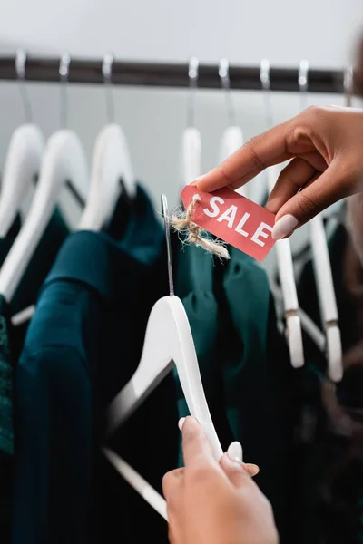 Abgeschnittene Ansicht einer afrikanisch-amerikanischen Verkäuferin, die einen Kleiderbügel mit Verkaufsetikett in einer Bekleidungsboutique hält — Stockfoto