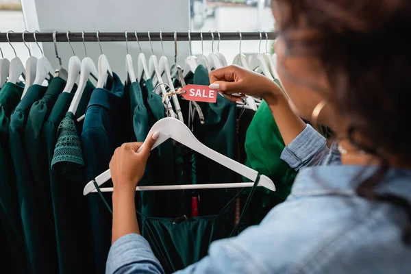 Verschwommen afrikanisch-amerikanische Verkäuferin hält Kleiderbügel mit Verkaufsetikett in Bekleidungsboutique — Stockfoto