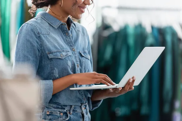 Vista recortada de la mujer afroamericana feliz usando el ordenador portátil en la boutique - foto de stock