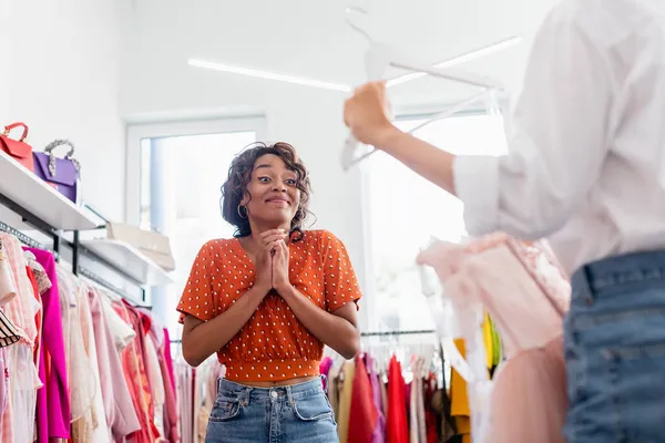 Joyeuse femme afro-américaine regardant un ami tenant une robe rose sur cintre — Photo de stock