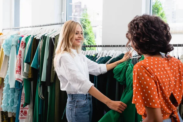 Amigos multiétnicos felices de pie cerca de la ropa verde en boutique — Stock Photo