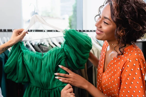 Happy african american woman holding green dress and looking at tattooed friend — Stock Photo