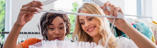 Amigos multiétnicos felices mirando el vestido en la percha en la boutique, bandera - foto de stock