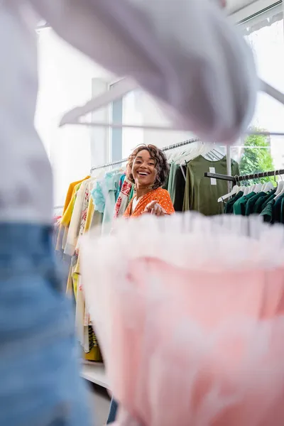 Alegre afroamericana mujer señalando borrosa vestido rosa cerca de amigo - foto de stock