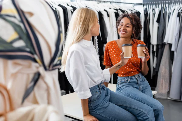 Amigos multiétnicos felices sosteniendo vasos de papel en boutique - foto de stock