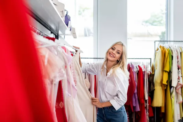 Mujer rubia feliz sosteniendo vestido rosa al elegir ropa - foto de stock