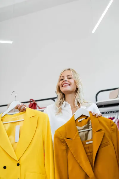 Glückliche und blonde Frau hält Kleiderbügel mit gelben Blazern — Stockfoto