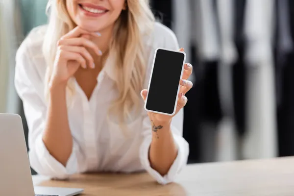 Vue recadrée de la vendeuse heureuse tenant smartphone avec écran blanc au comptoir de vente — Photo de stock