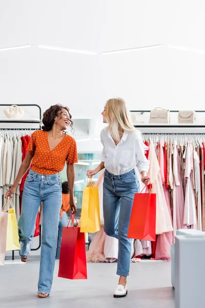 Feliz interracial mulheres segurando sacos de compras em roupas boutique — Fotografia de Stock