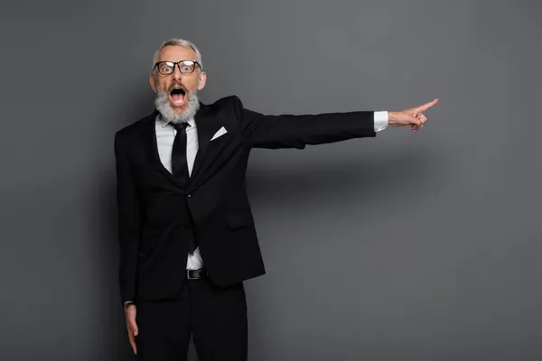 Sorprendido hombre de negocios de mediana edad en gafas apuntando con el dedo en gris - foto de stock