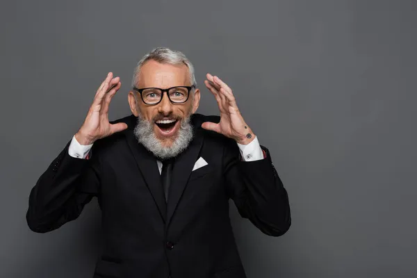 Verblüffter Geschäftsmann mittleren Alters mit Brille gestikuliert auf grau — Stockfoto