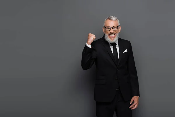 Збуджений бізнесмен середнього віку в окулярах радіє ізольовано на сірому — стокове фото