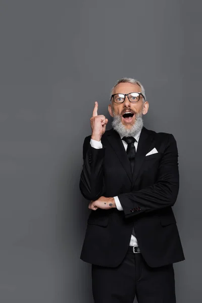 Sorprendido hombre de negocios de mediana edad en gafas apuntando con el dedo mientras tiene idea aislada en gris - foto de stock