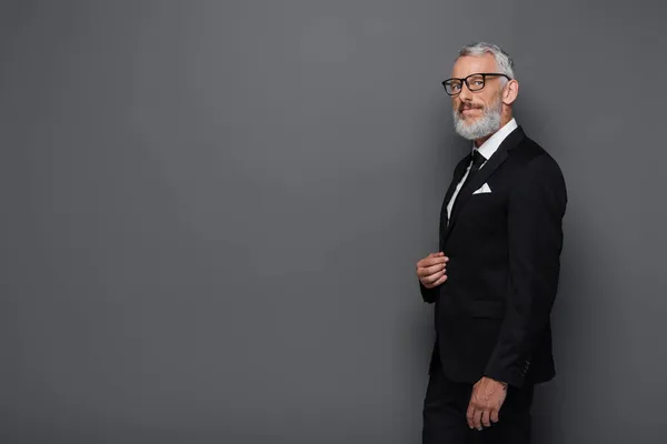 Pleased middle aged businessman in glasses and suit isolated on grey — Stock Photo