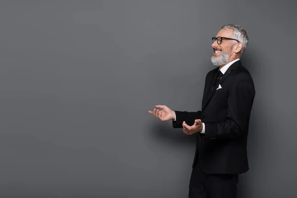 Empresario positivo de mediana edad en gafas y traje riendo en gris - foto de stock