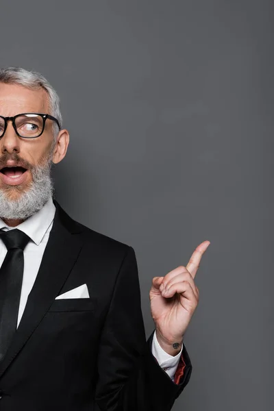 Vista recortada de empresario sorprendido de mediana edad en gafas y traje apuntando con el dedo en gris - foto de stock