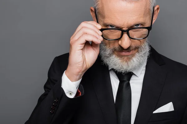 Sérieux homme d'affaires d'âge moyen réglage des lunettes tout en regardant la caméra isolée sur gris — Photo de stock