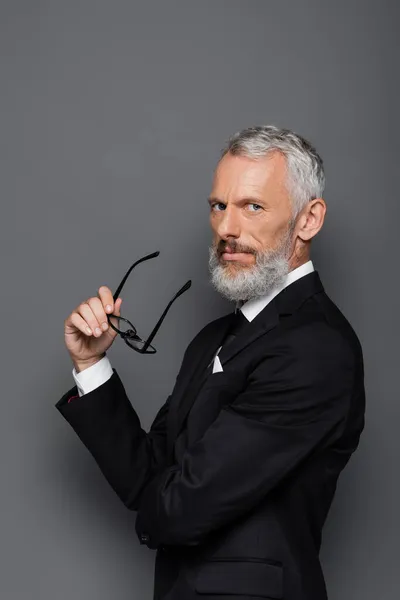 Homem de negócios de meia idade em terno segurando óculos em cinza — Fotografia de Stock