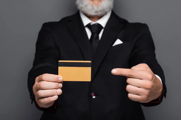 Обрезанный вид бородатого бизнесмена средних лет в костюме, указывающий на кредитную карту, изолированную на сером — стоковое фото