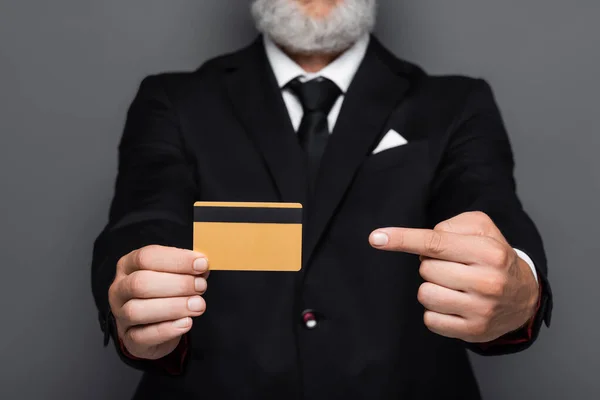 Cropped view of bearded middle aged businessman in suit pointing at credit card isolated on grey — Stock Photo