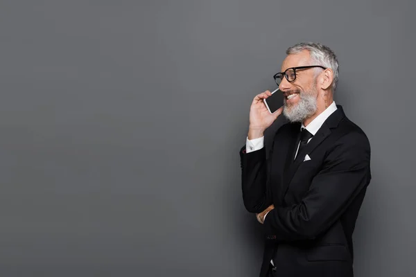 Веселый бизнесмен средних лет разговаривает по мобильному телефону на сером — стоковое фото