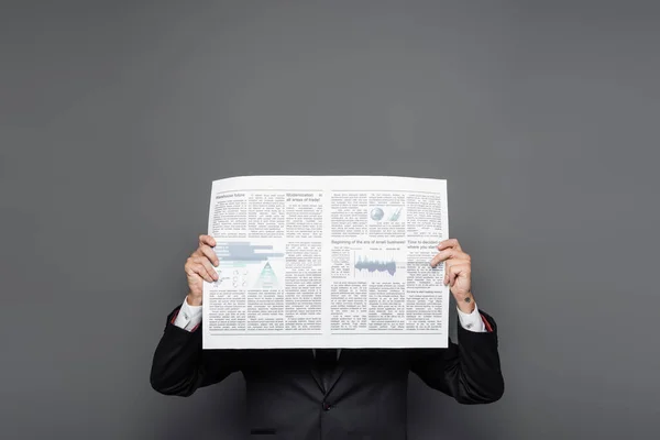 Middle aged businessman obscuring face with newspaper on grey — Stock Photo