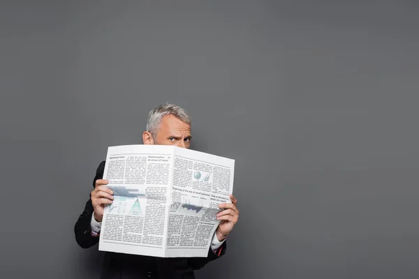 Uomo d'affari di mezza età che copre il viso con il giornale su grigio — Foto stock